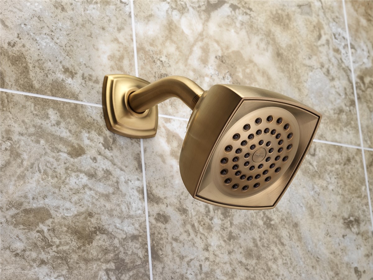 Close-up of a bronze square showerhead mounted on a textured, light-brown tiled wall, showcasing modern bathroom design.