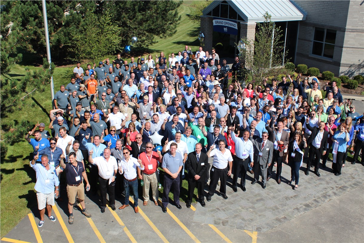 A diverse group of people stands together in front of a large building, smiling and engaging with one another.