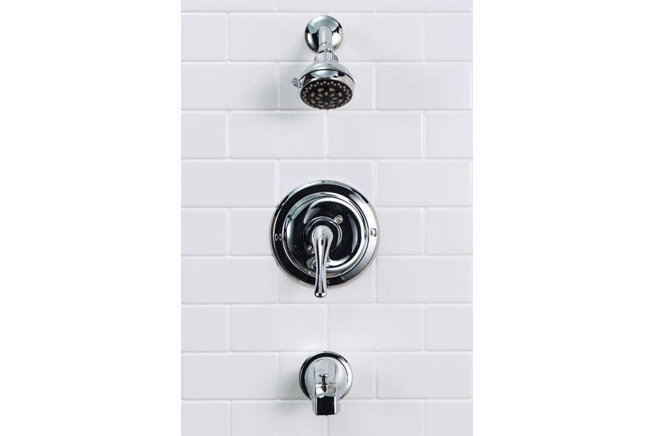 Chrome shower fixtures including a shower head, shower control, and spout installed on a white-tiled wall.