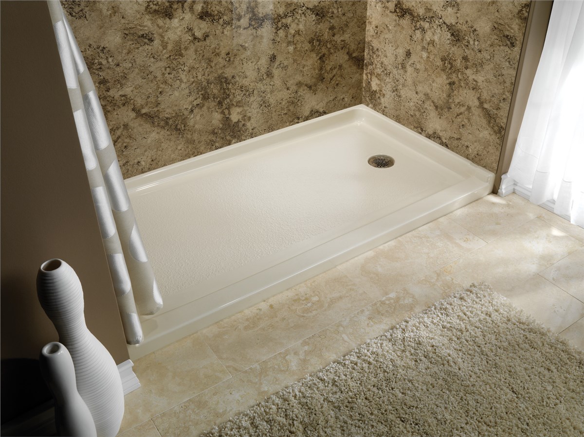 Low-threshold ivory shower base with a drain, next to brown speckled wall paneling, ivory tile flooring, and a plush rug.