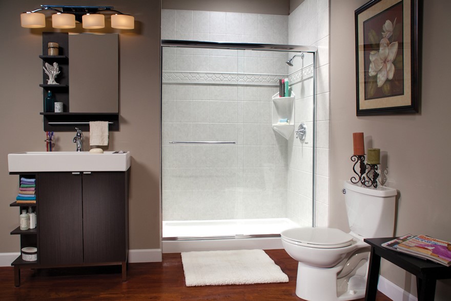 Modern bathroom with a sink and vanity on the left, a glass-enclosed shower in the center, a toilet on the right, and a side table with magazines; neutral wall colors and framed floral artwork.