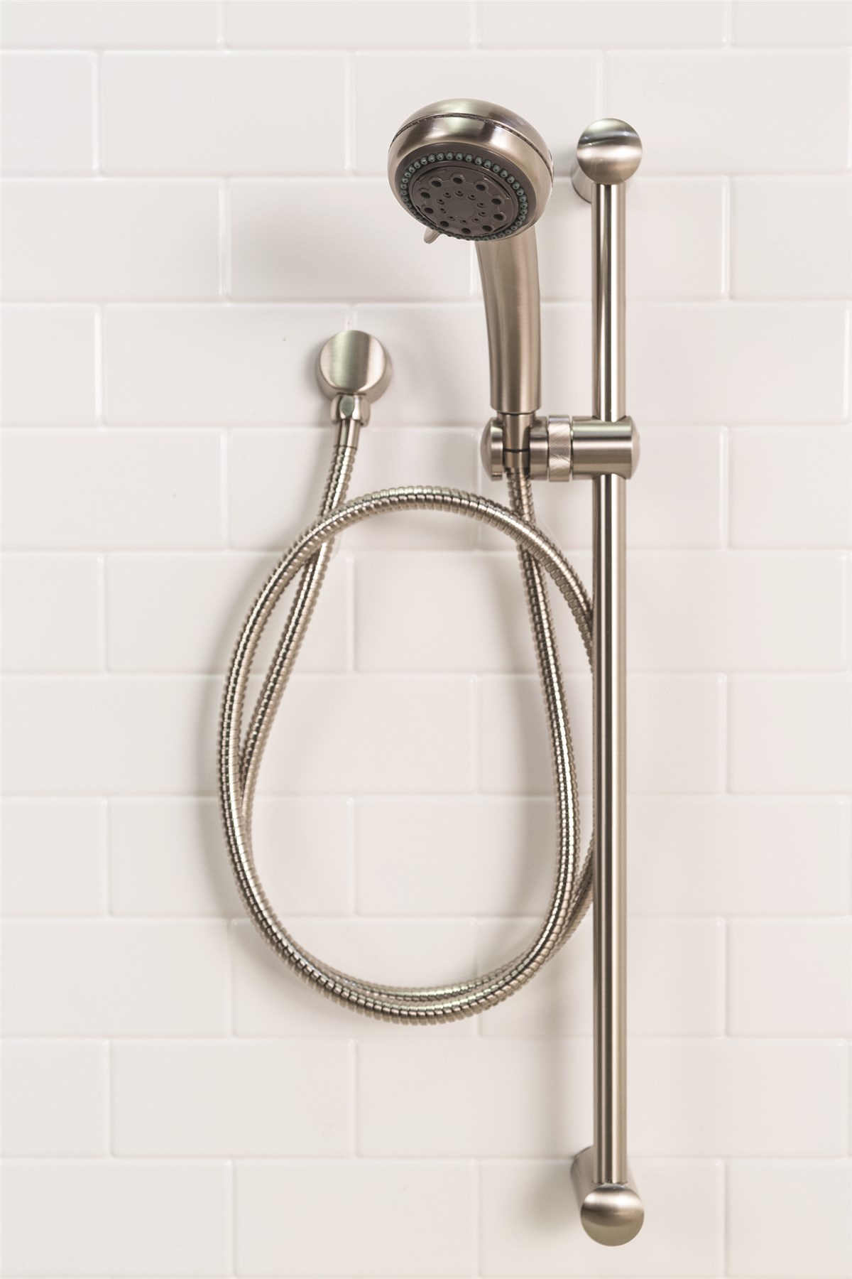 Wall-mounted showerhead with a flexible hose and sliding bar, set against a white tiled background. Modern, sleek design.