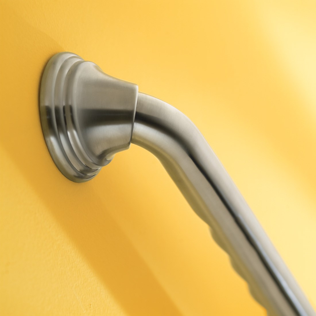 Brushed metal grab bar mounted on a yellow wall.