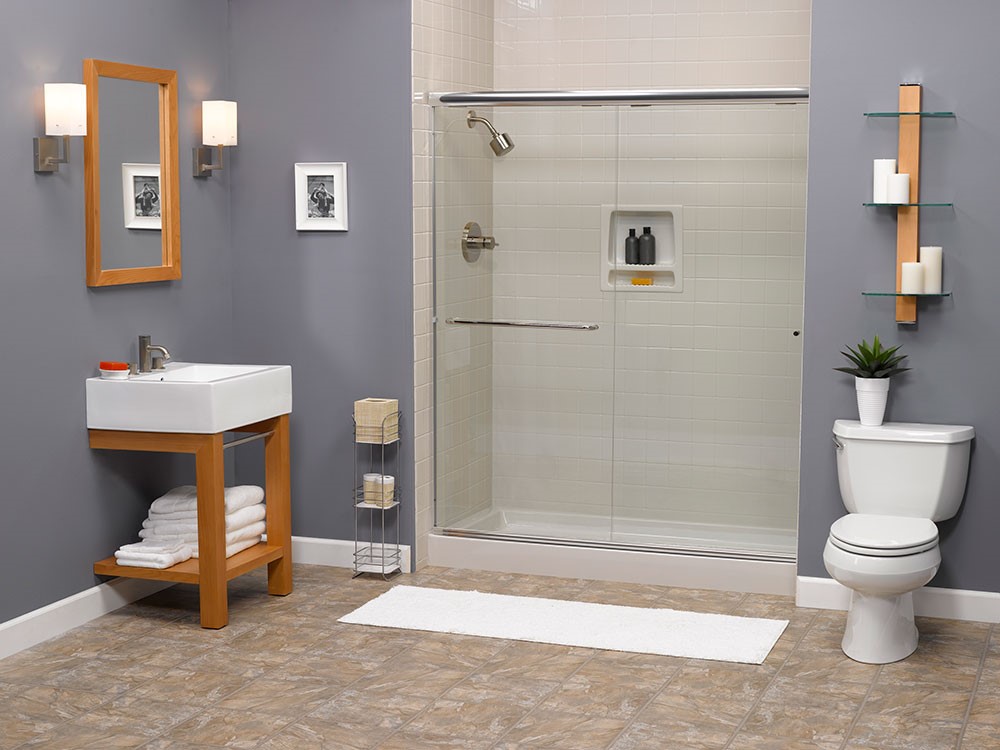 Interior bathroom showcasing a sink with wood frame, a glass-doored shower, and a toilet, complemented by a framed mirror and shelving with decorative candles and a plant.