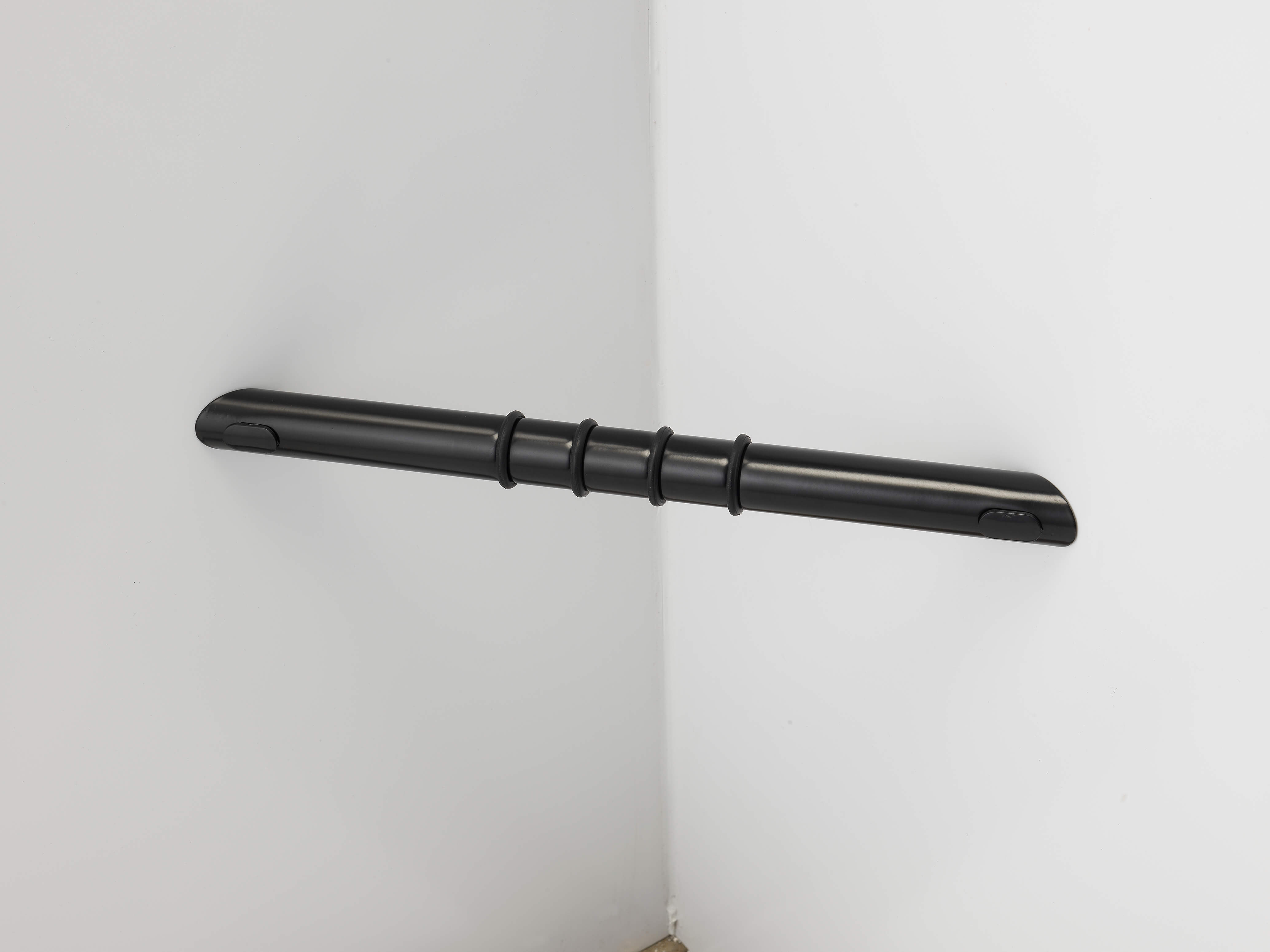 A black grab bar with three raised grips is mounted horizontally across the corner of two white walls.