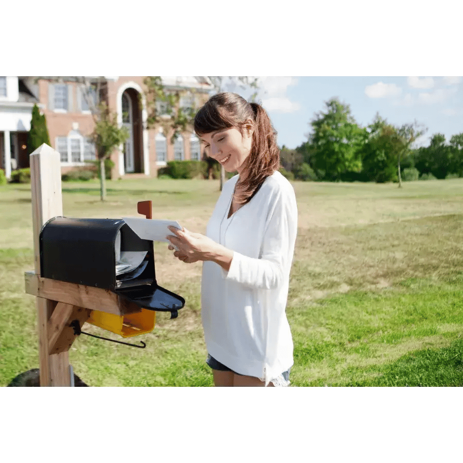Woman standing in front of a mailbox removing mail, with a slight smile, on a sunny day in front of a house.