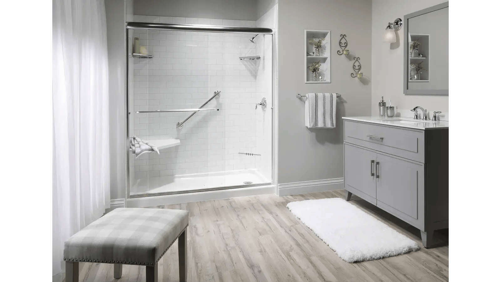 Bathroom featuring a tiled shower with grab bars and a built-in seat, a grey vanity, and neutral-toned flooring.