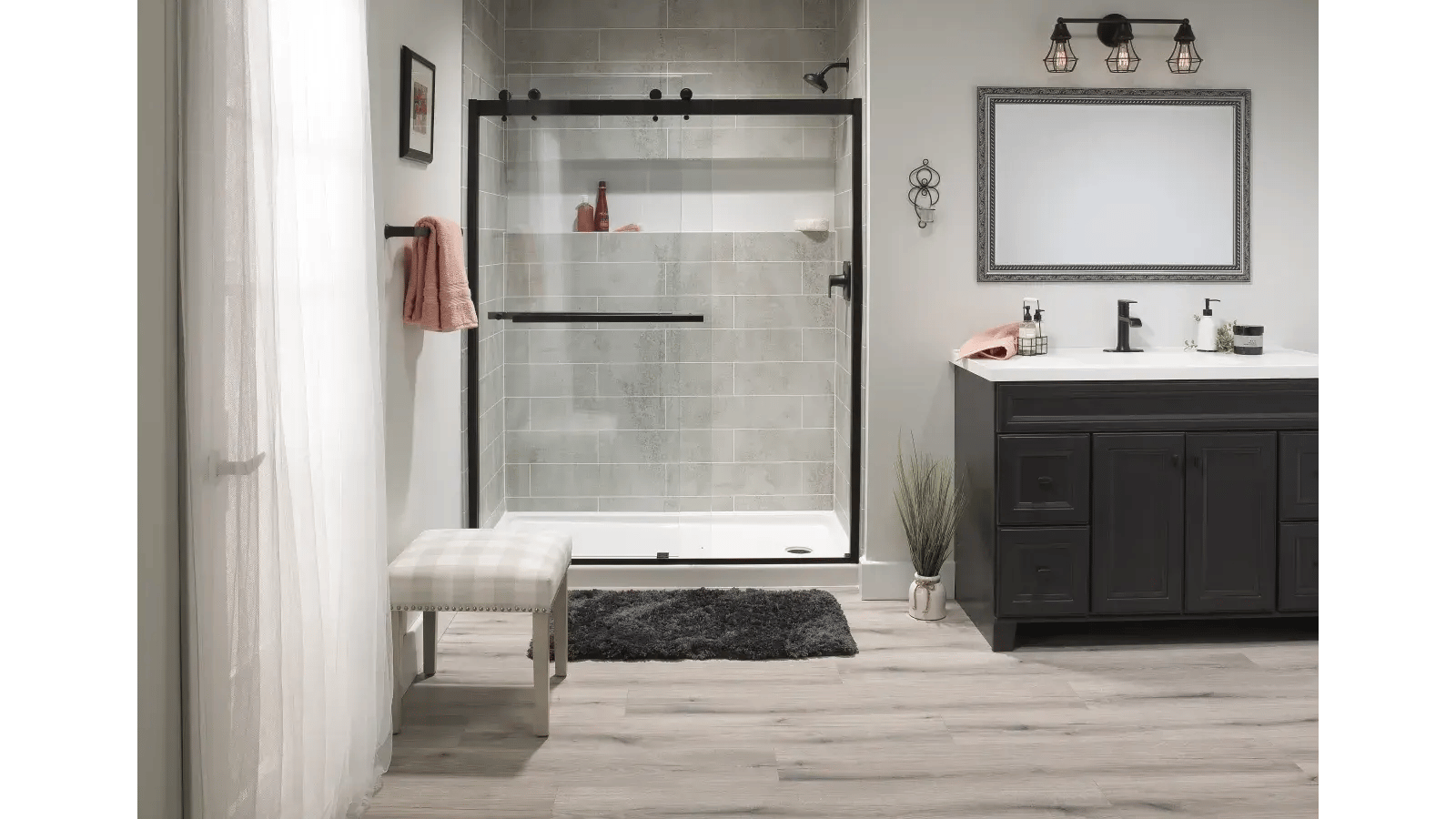 Modern bathroom design featuring a black-framed glass shower stall with grey tiled walls, a vanity with a light-colored countertop, a framed mirror, and a window with translucent curtains.
