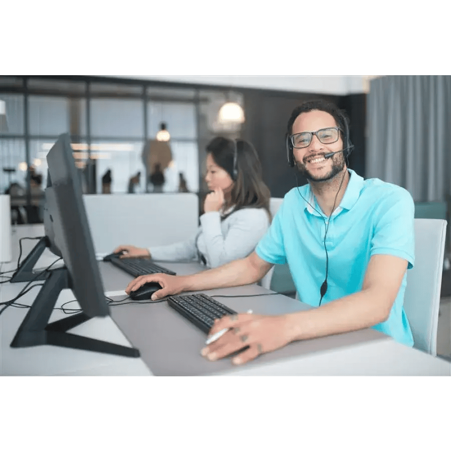 Smiling man wearing a headset works at a computer in an office alongside a woman using a computer.