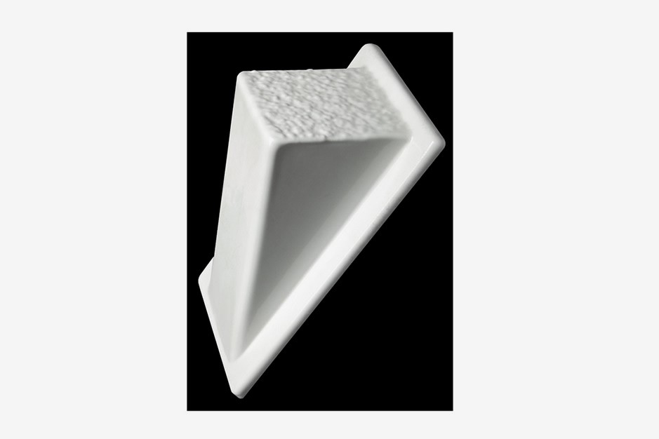 A white, wedge-shaped ceramic object with a textured top surface, displayed against a solid black background.