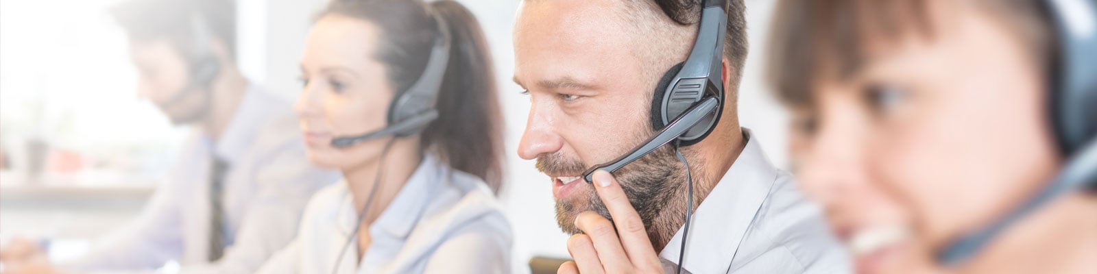 Four customer service representatives wearing headsets are visible, with the closest agent appearing to speak into the microphone.