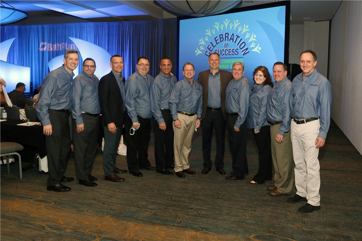 A group of ten smiling people pose in front of a screen that reads Celebration of Success Conference Awards and Gala