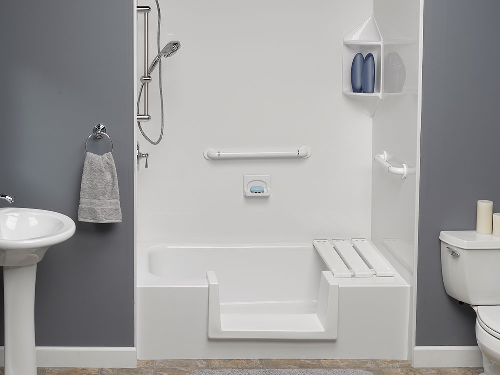 Accessible bathroom featuring a white walk-in bathtub with a seat, a gray wall, a pedestal sink, and a toilet.